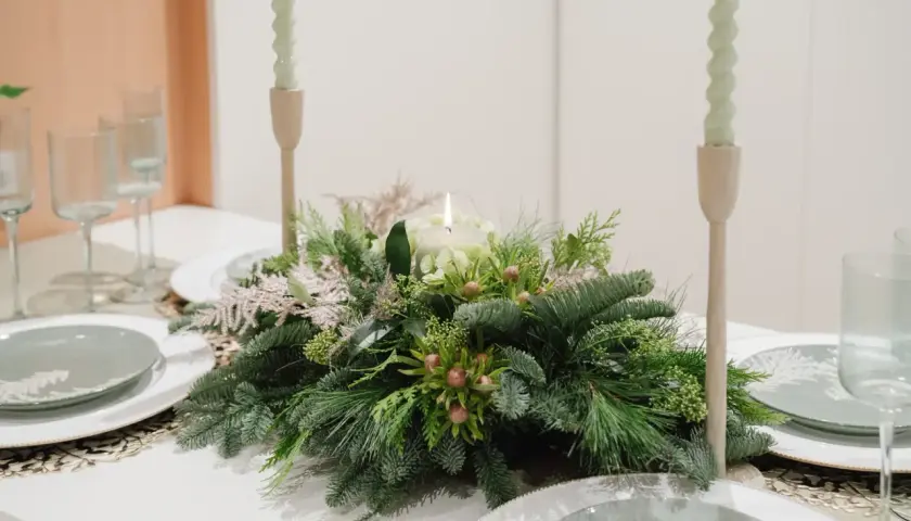 Centros de mesa de navidad sencillas con velas y follaje verde. Copas y platos listos para una cena festiva.