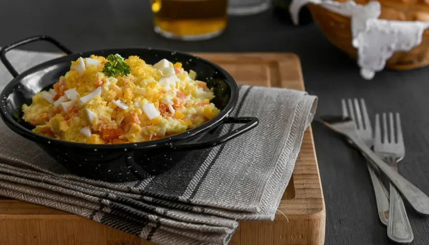 Deliciosa ensaladilla rusa en un cuenco negro, con huevo duro picado y perejil. Acompañada de pan y cerveza.