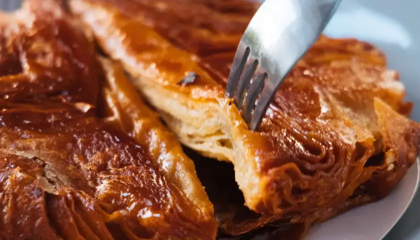 Un tenedor se hunde en un crujiente y caramelizado kouign amann, revelando sus capas hojaldradas.