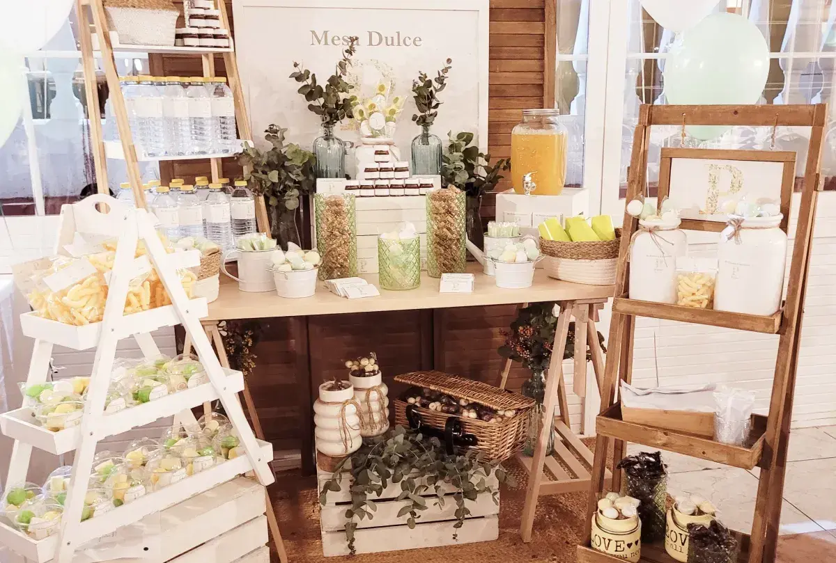 Mesa dulce con dulces, botellas de agua y un dispensador de jugo. Ideas para como hacer un candy bar.