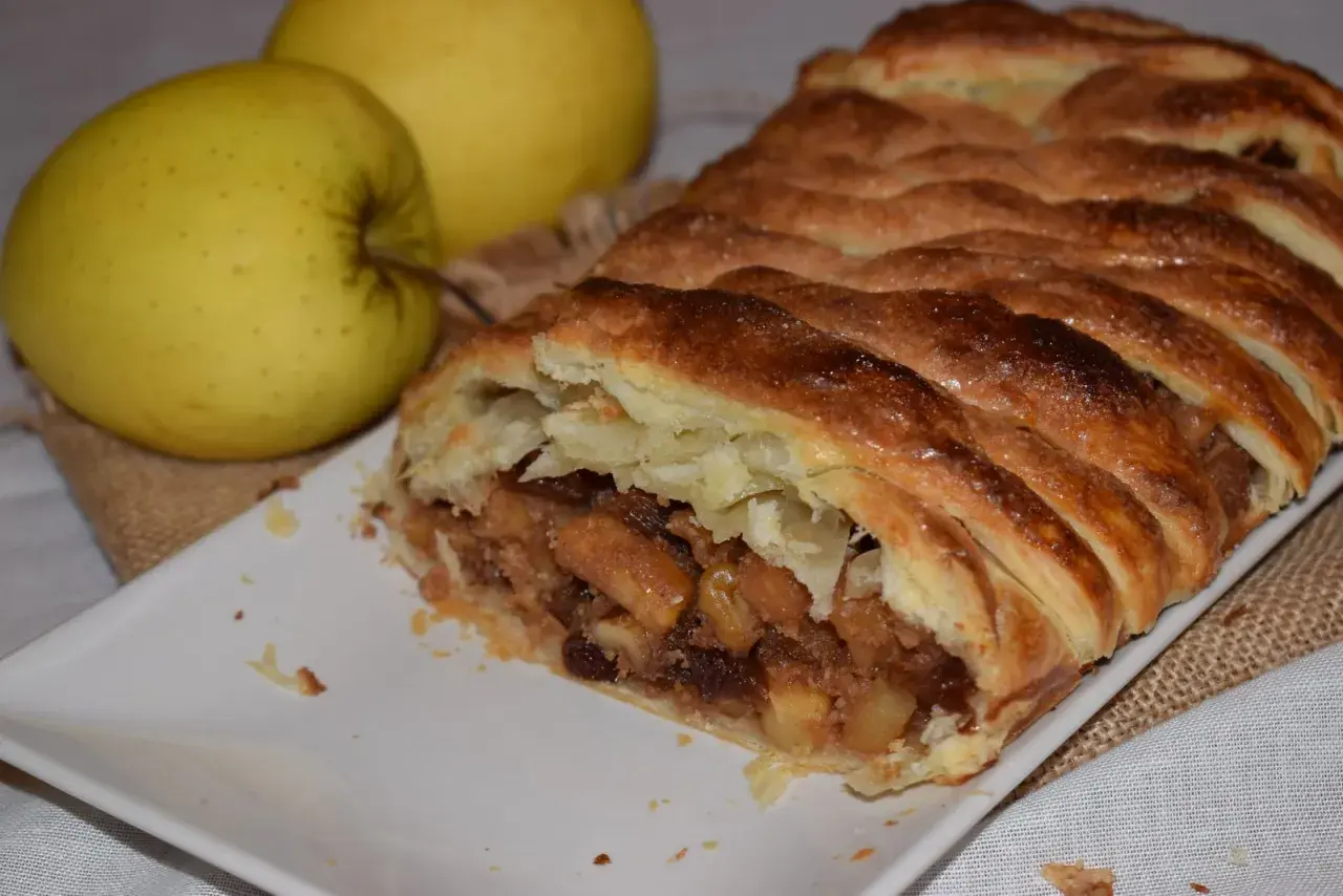 Un delicioso strudel de manzana recién horneado, con su masa dorada y crujiente, relleno de trozos de manzana y pasas.