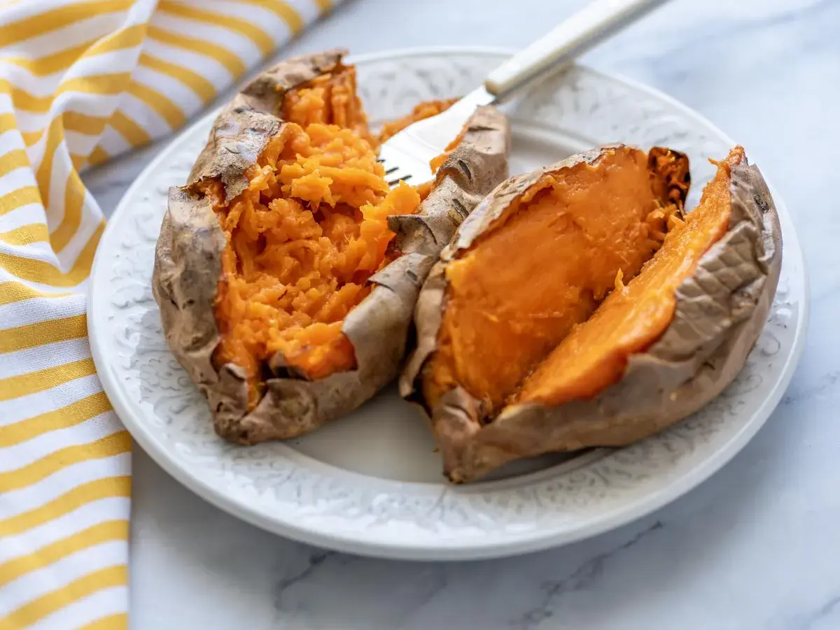 Dos mitades de boniato asado en freidora de aire, servidas en un plato blanco con un tenedor.