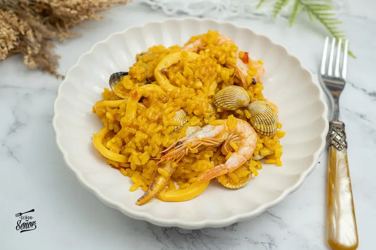 Deliciosa paella de marisco, con gambas, calamares y mejillones, servida en un plato blanco.