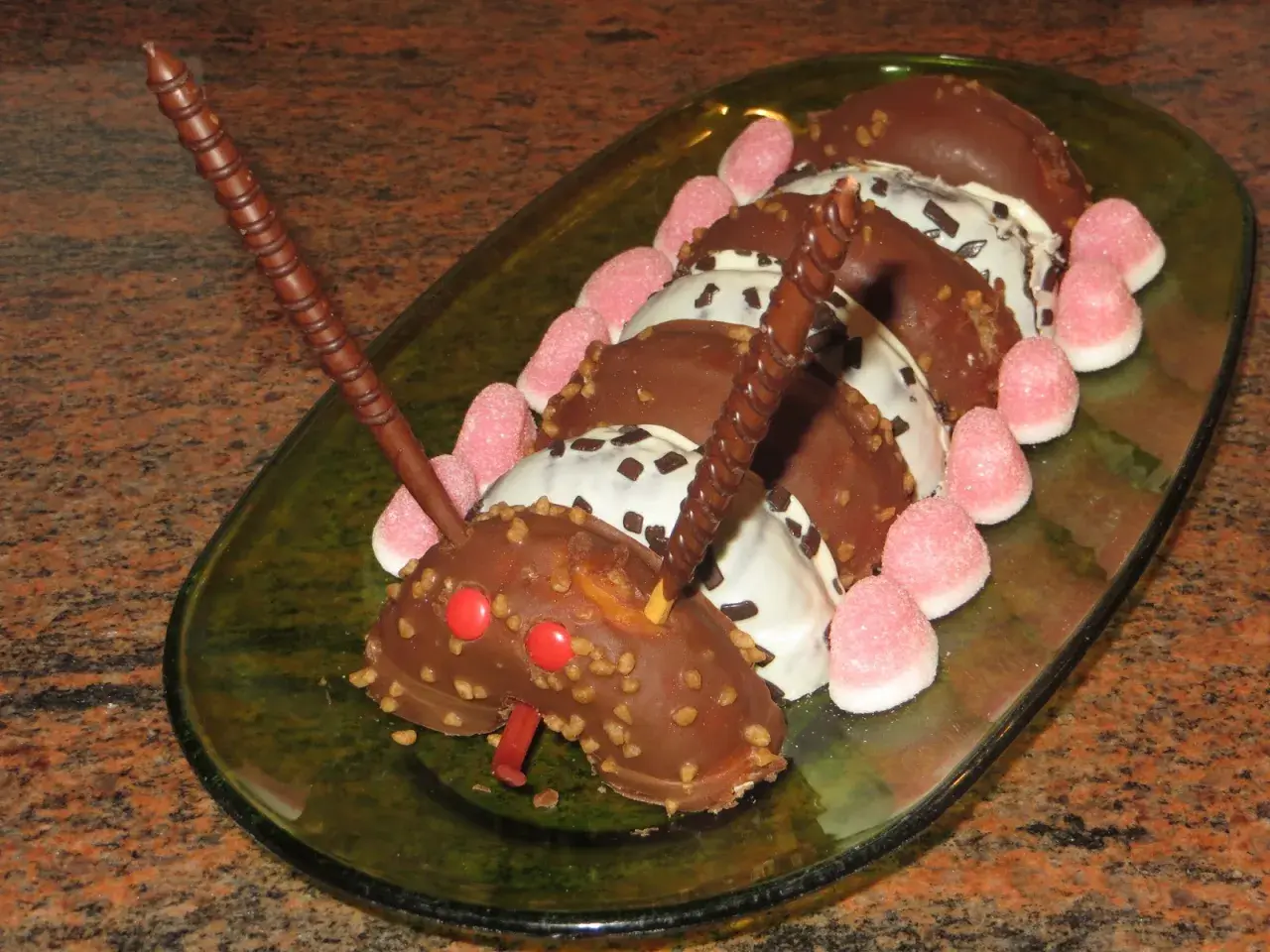 Tarta infantil con forma de oruga hecha de donuts cubiertos de chocolate, decorada con gominolas rosas y barquillos de chocolate.