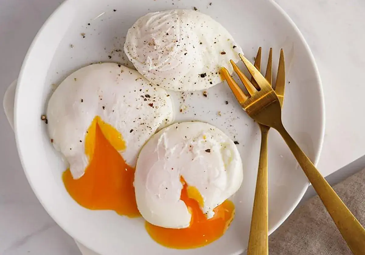Tres huevos poche perfectamente cocidos, con la yema líquida y dorada, espolvoreados con pimienta negra, listos para disfrutar.