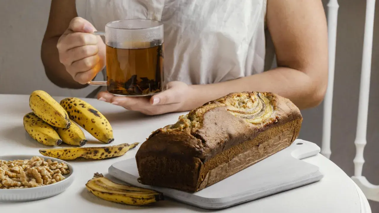 Un delicioso banana bread recién horneado, acompañado de plátanos maduros, nueces y una taza de té humeante.