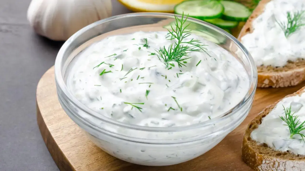 Un tazón de cremosa salsa de yogur con eneldo fresco, perfecto para untar en pan tostado.