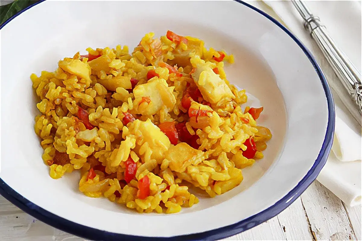 Un plato de arroz con bacalao, pimientos rojos y trozos de pescado blanco. Un delicioso arroz con bacalao listo para disfrutar.