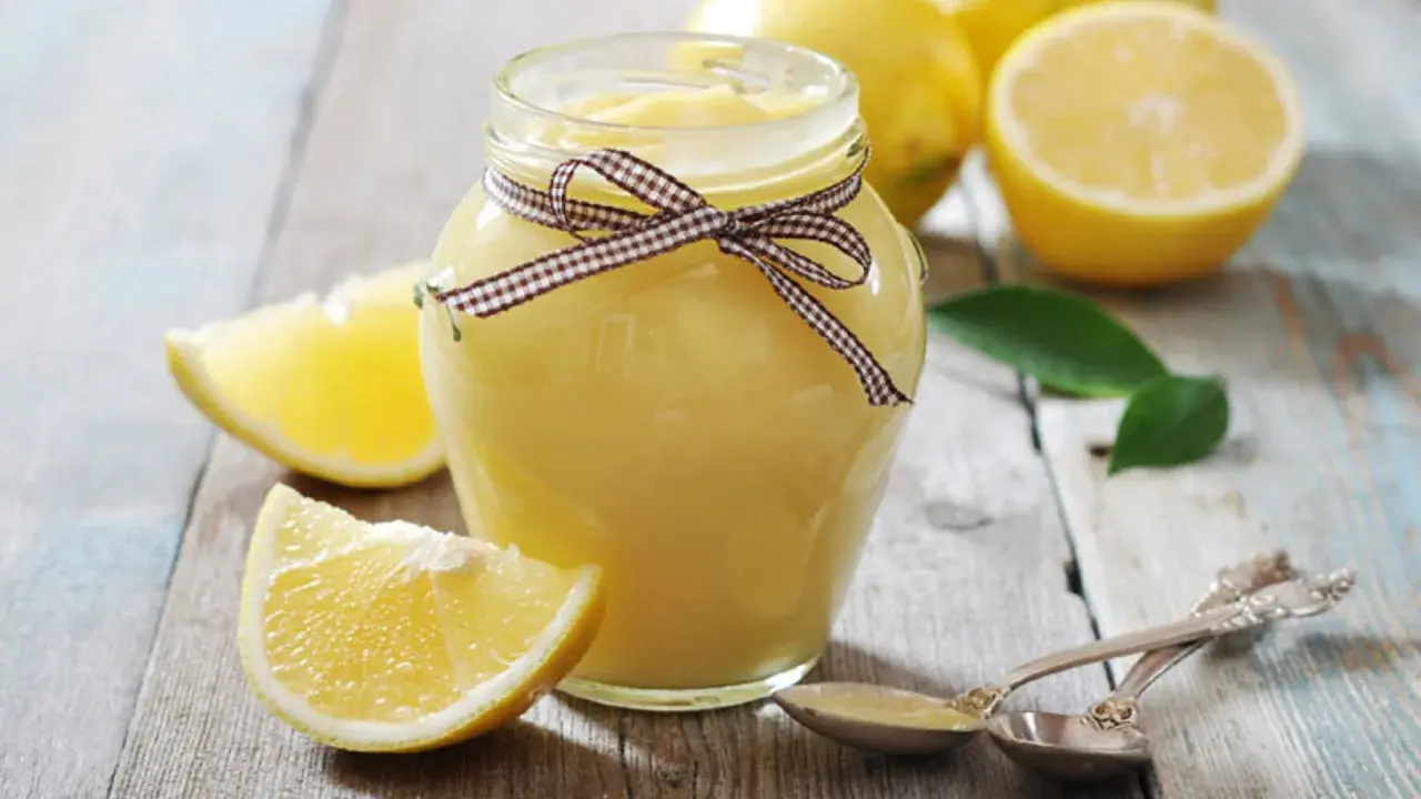 Tarro de lemon curd casero, decorado con un lazo, rodeado de limones frescos y rodajas.