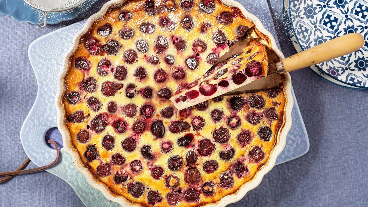 Un delicioso clafoutis de cerezas recién horneado, con una porción servida, espolvoreado con azúcar glas.
