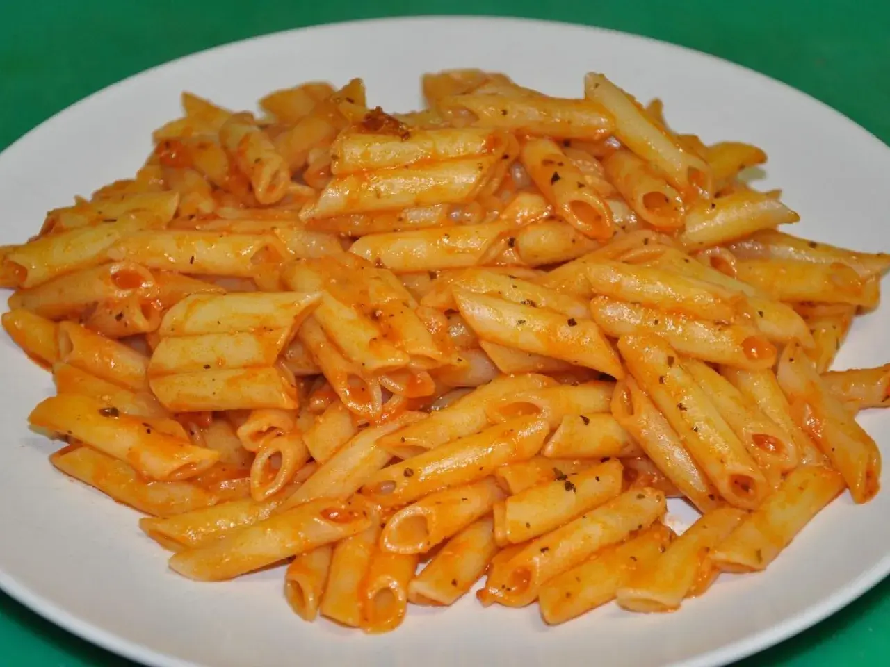 Un plato blanco lleno de macarrones con tomate, cubiertos con una salsa roja y especias.
