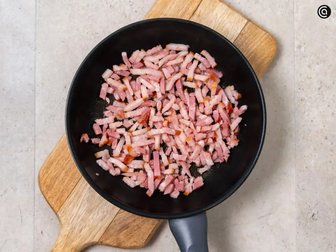 Trozos de bacon crudo en una sartén negra sobre una tabla de madera. Preparando la base para una deliciosa mermelada de bacon.