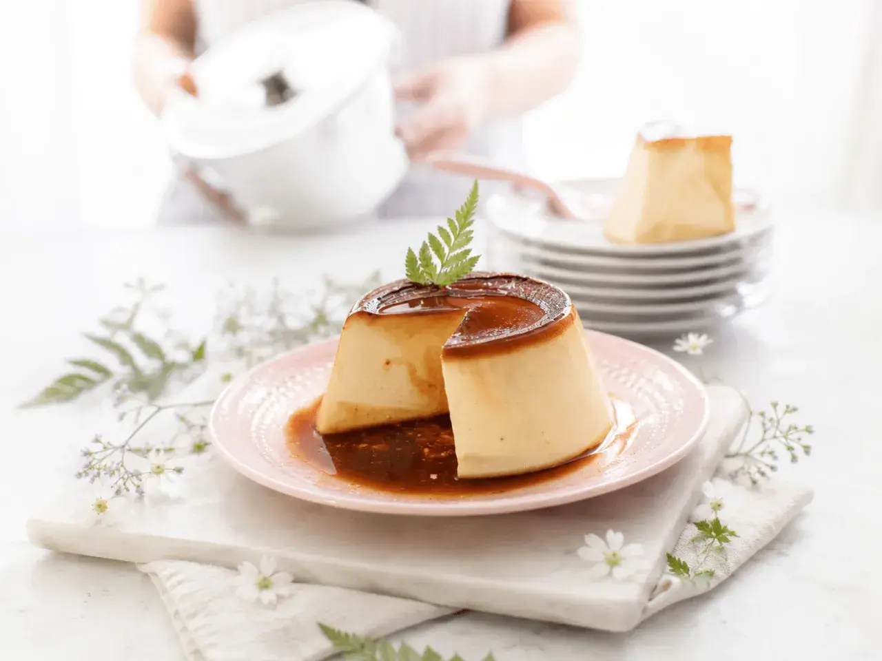 Delicioso flan de queso con caramelo líquido, decorado con una hoja verde y flores delicadas.