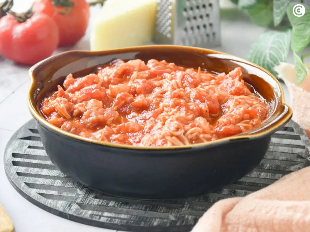 Un tazón de pasta amatriciana, con tomates frescos, queso y rallador al fondo.