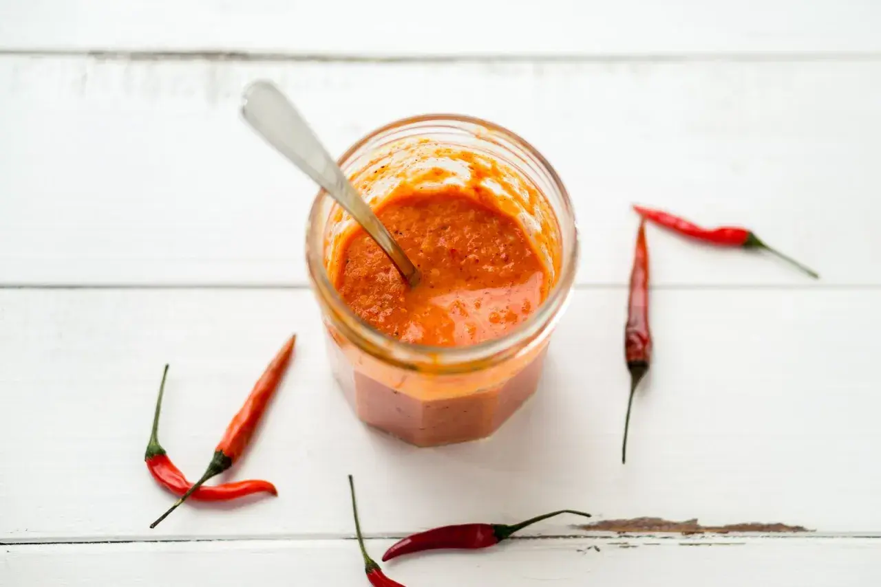 Tarro de cristal con salsa piri piri y chiles rojos alrededor, listo para dar un toque picante a tus platos.