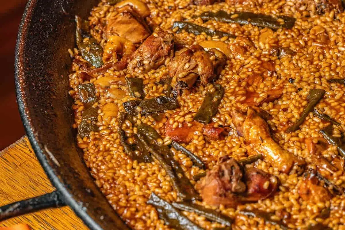 Paella de pollo y judías verdes, con el arroz ligeramente quemado en el fondo, creando un socarrat crujiente.