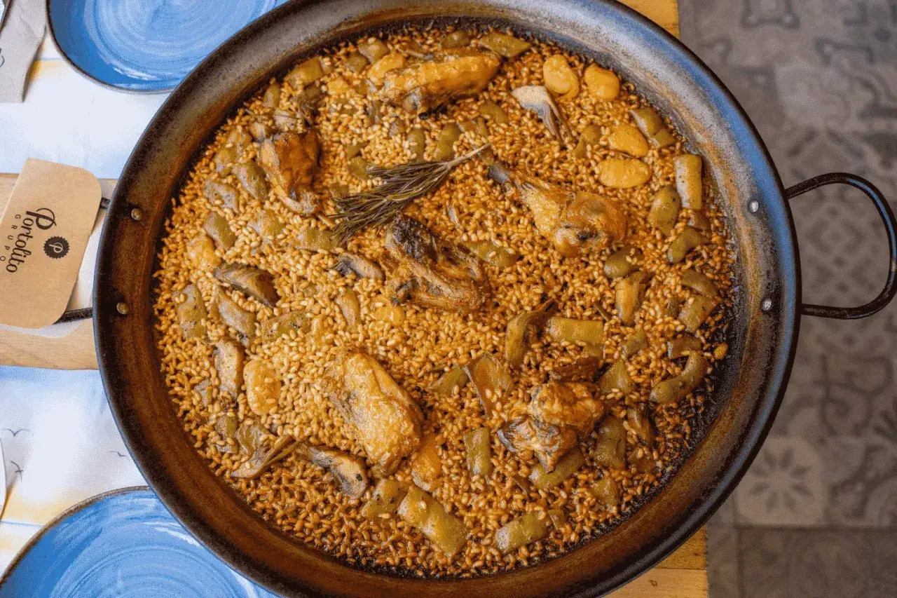Paella valenciana que lleva pollo, conejo y verduras, con un toque de romero. Un plato tradicional y delicioso.
