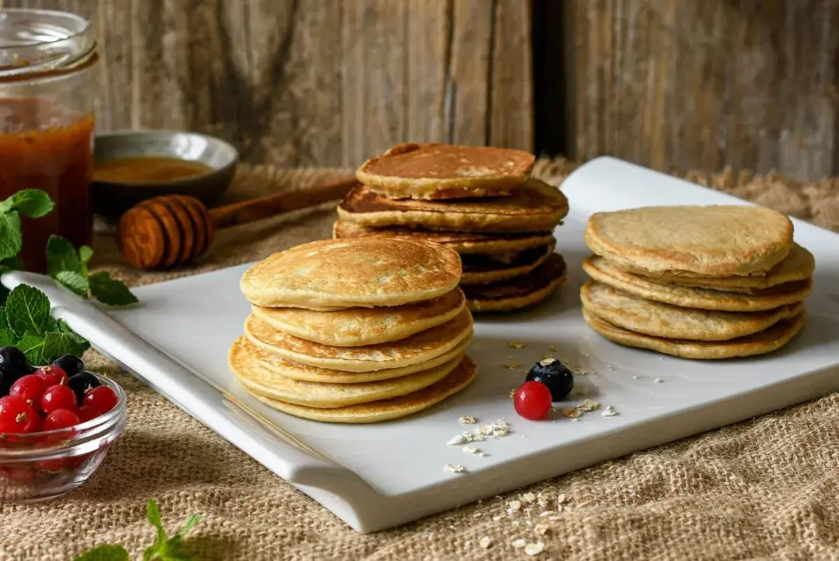 Montón de tortitas de avena doradas, servidas con frutos rojos y miel. Un desayuno perfecto.