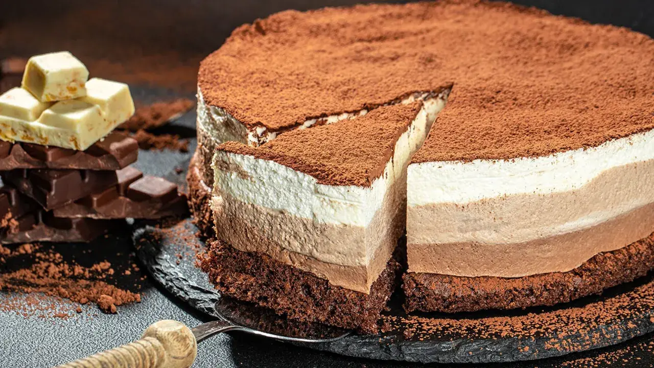 Tarta de tres chocolates, con capas de mousse de chocolate blanco, con leche y negro, espolvoreada con cacao.
