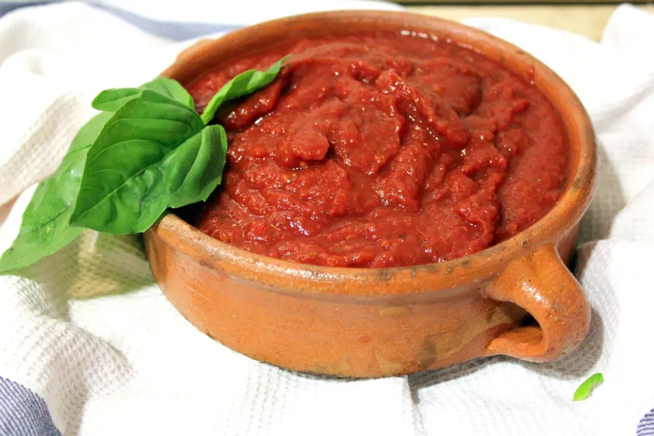 Salsa napolitana casera en cazuela de barro, decorada con hojas de albahaca fresca.