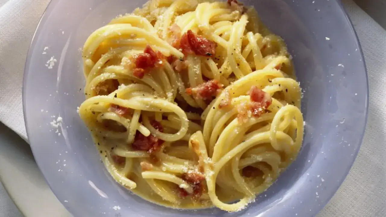 Un plato de pasta carbonara cremoso, con trozos de panceta crujiente y espolvoreado con queso rallado.