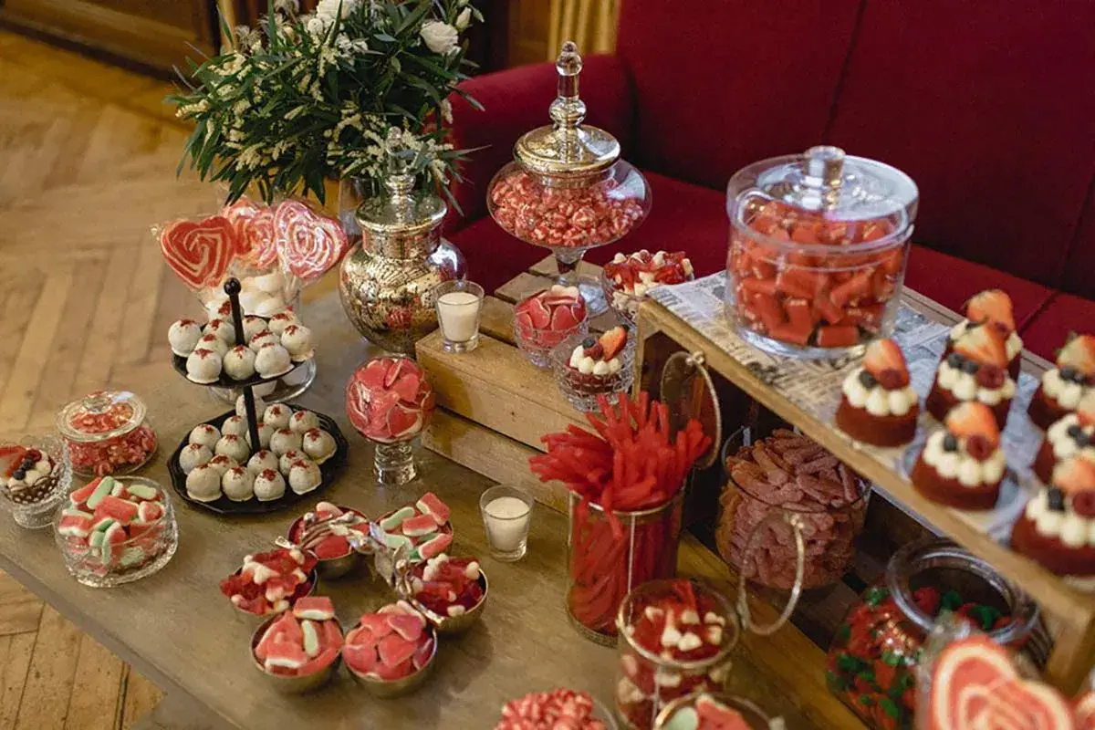 Ideas para como hacer un candy bar para boda: mesa llena de dulces rojos y blancos, pasteles, caramelos y piruletas en forma de corazón.