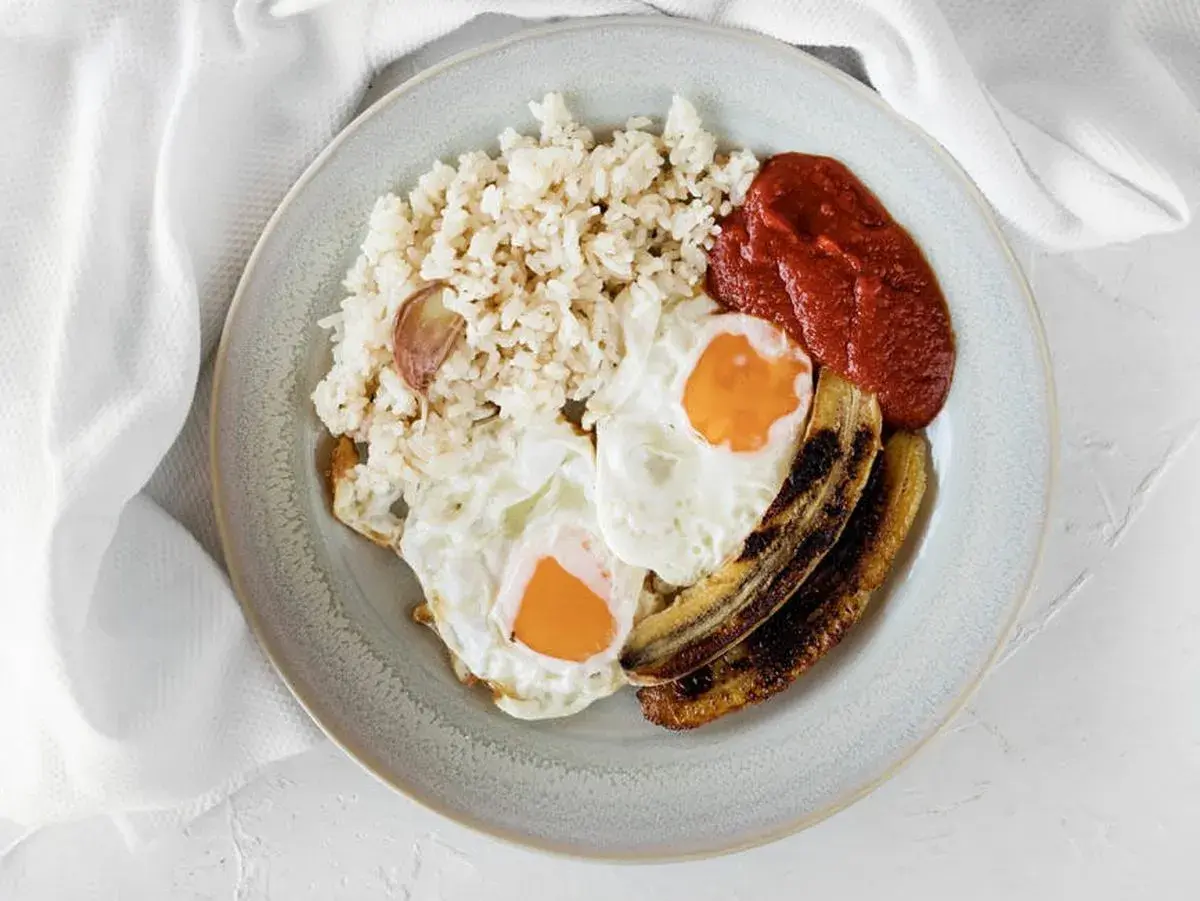Un plato de arroz a la cubana con dos huevos fritos, plátano maduro frito y salsa de tomate.