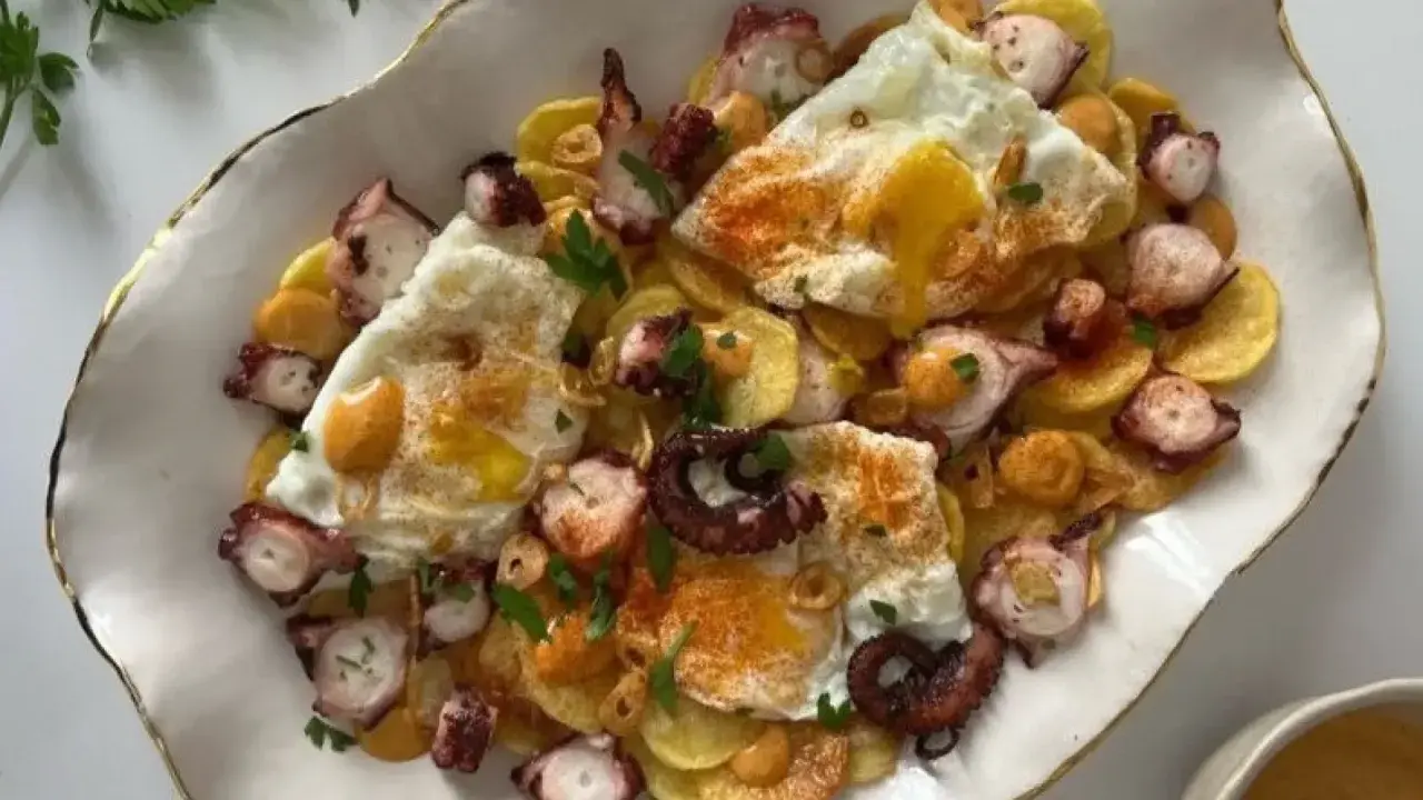 Delicioso plato de pulpo con patatas y huevos rotos, espolvoreado con pimentón y perejil.