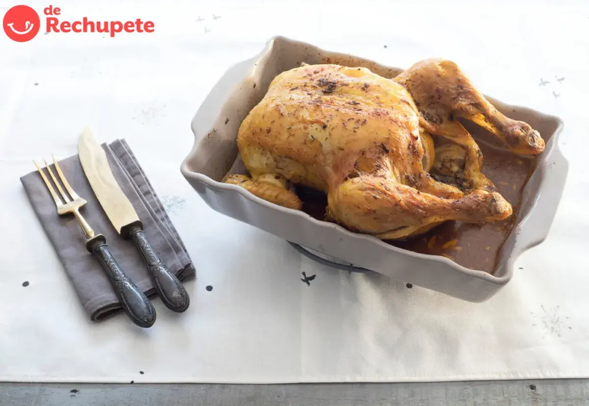 Pollo asado dorado en una fuente, listo para servir. Ideal para tus recetas con pollo. Cubiertos y servilleta a un lado.