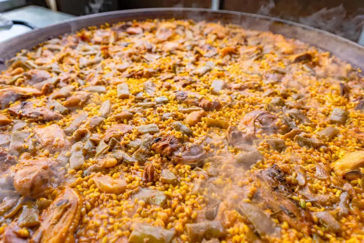 Paella humeante con pollo, judías verdes y trozos de carne. El arroz bomba es el que mejor absorbe el sabor, ideal para esta paella.