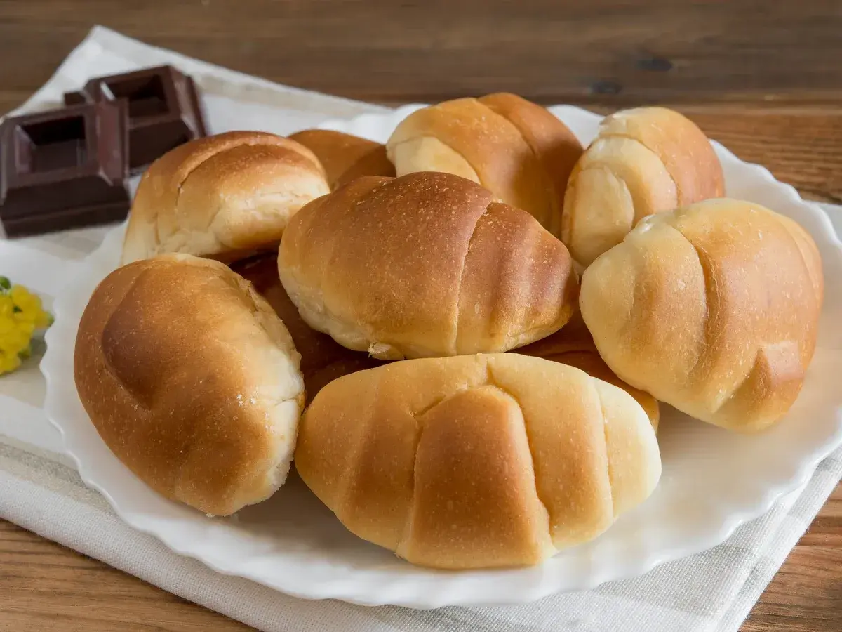 Un plato blanco con pan de leche dorado y suave, junto a trozos de chocolate oscuro.