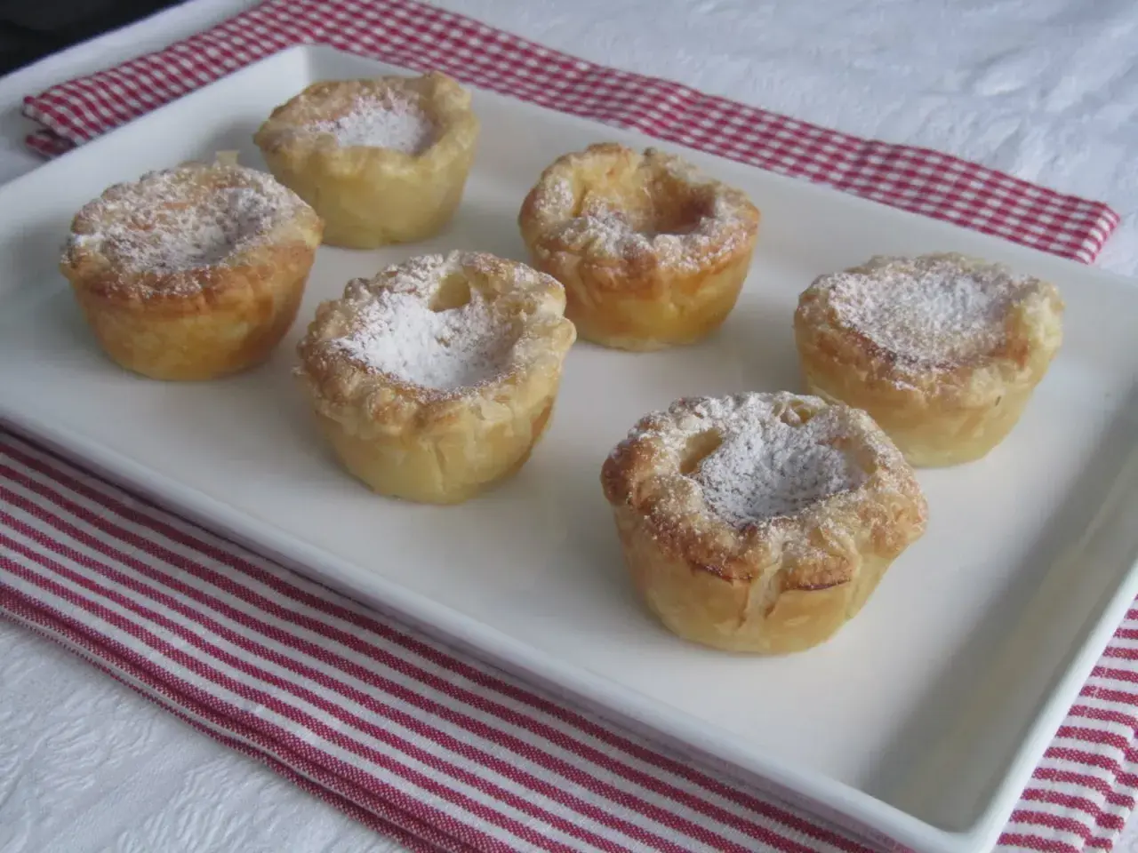 Seis pastelitos de arroz dorados, espolvoreados con azúcar glas, en una bandeja blanca.