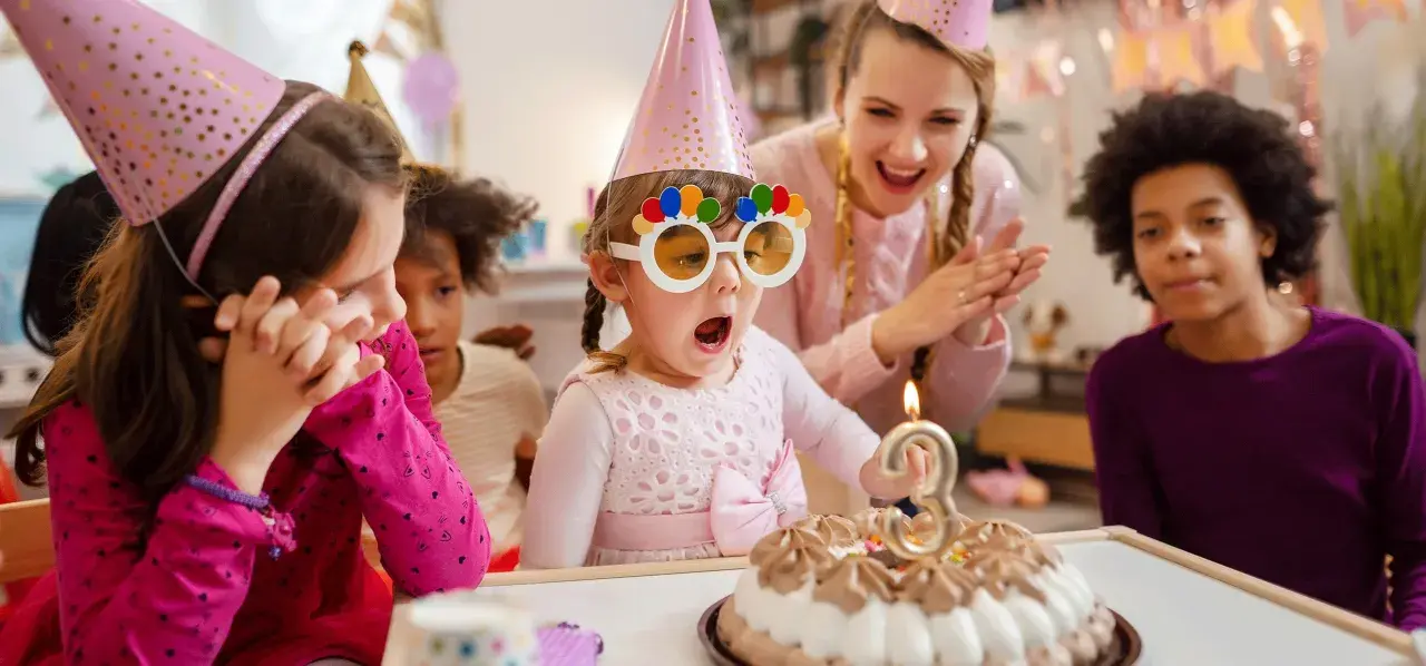 Niños celebran un cumpleaños con pastel y velas. La cumpleañera, con gafas divertidas, sopla la vela. Una temática de cumpleaños para niños llena de alegría.