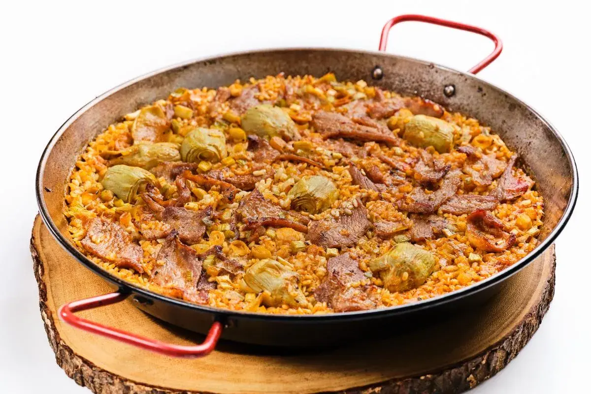 Arroz al horno con trozos de carne y alcachofas, servido en paellera sobre tabla de madera.