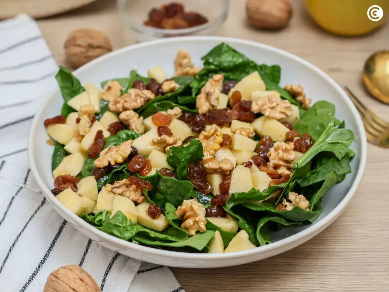 Deliciosa ensalada de espinacas con trozos de manzana, pasas y nueces crujientes.