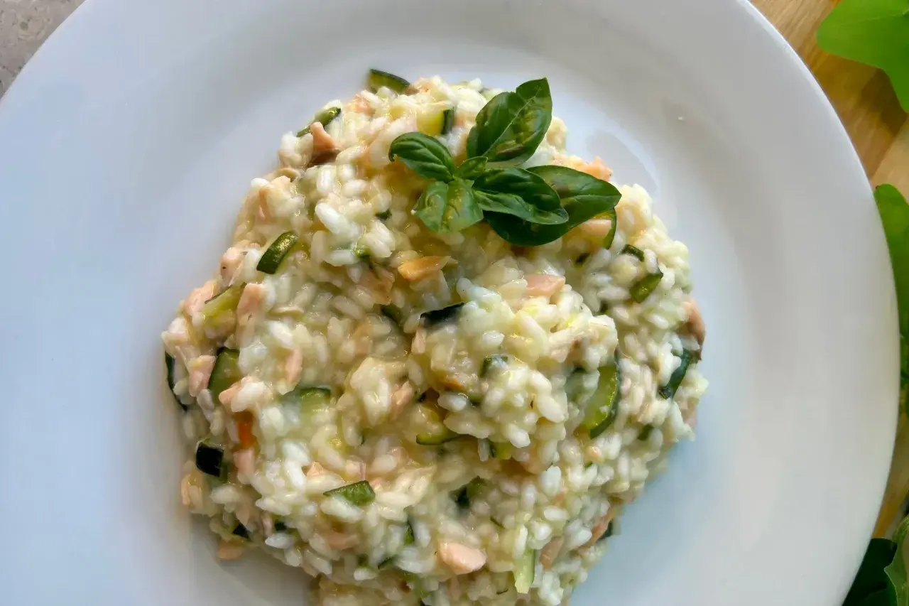 Cremoso arroz a la milanesa con salmón y calabacín, adornado con hojas de albahaca fresca.