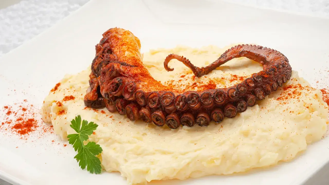 Delicioso pulpo a la plancha con puré cremoso, espolvoreado con pimentón y adornado con perejil fresco.