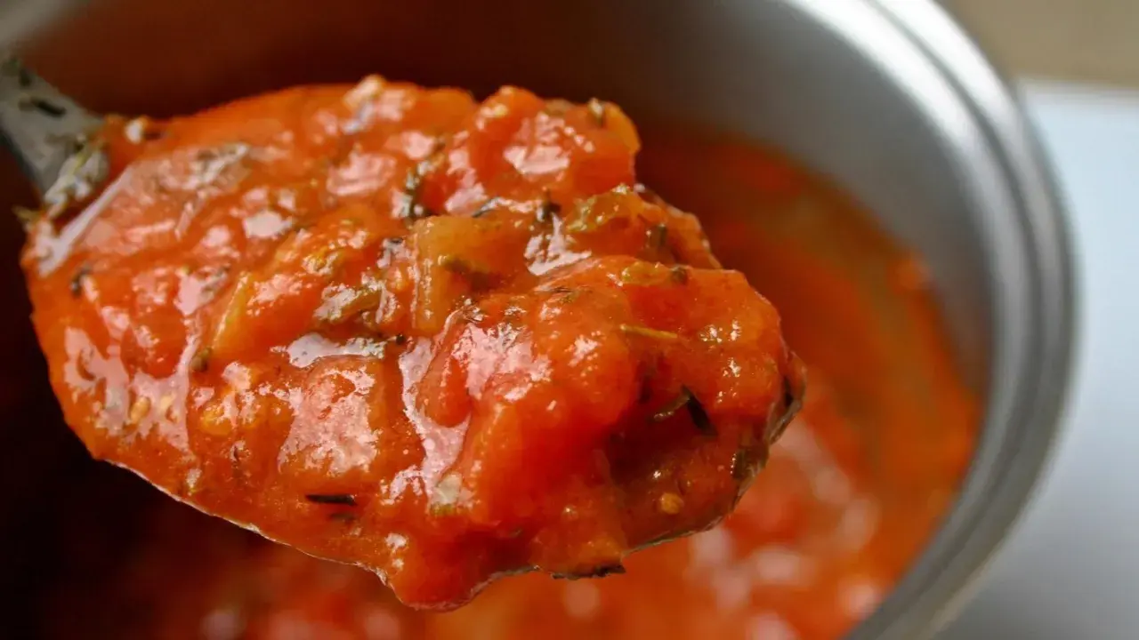 Cuchara llena de sabrosa salsa de tomate casera, con trozos de tomate y hierbas.