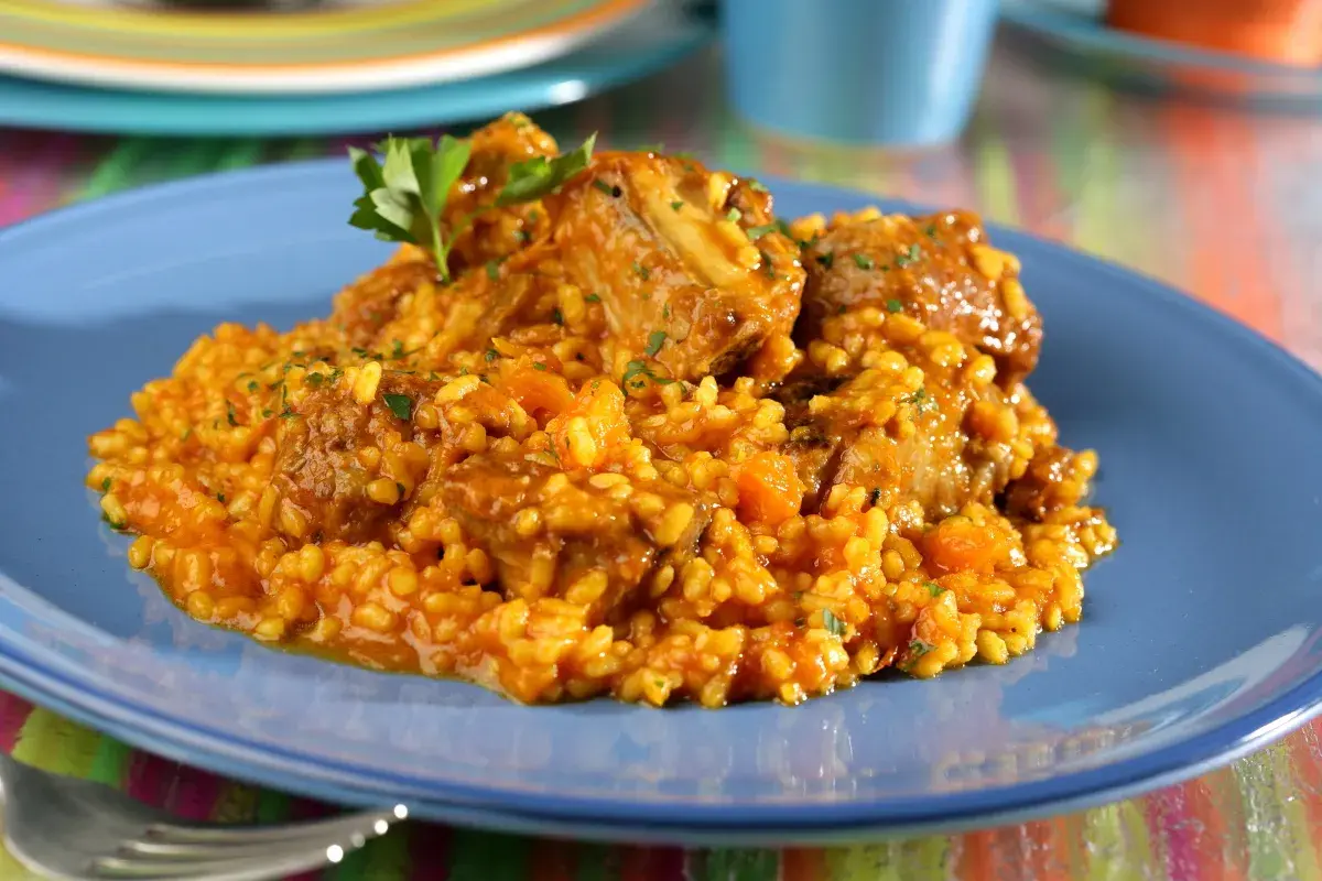 Arroz con costillas, un plato reconfortante con trozos de carne tierna y arroz amarillo, decorado con perejil fresco.