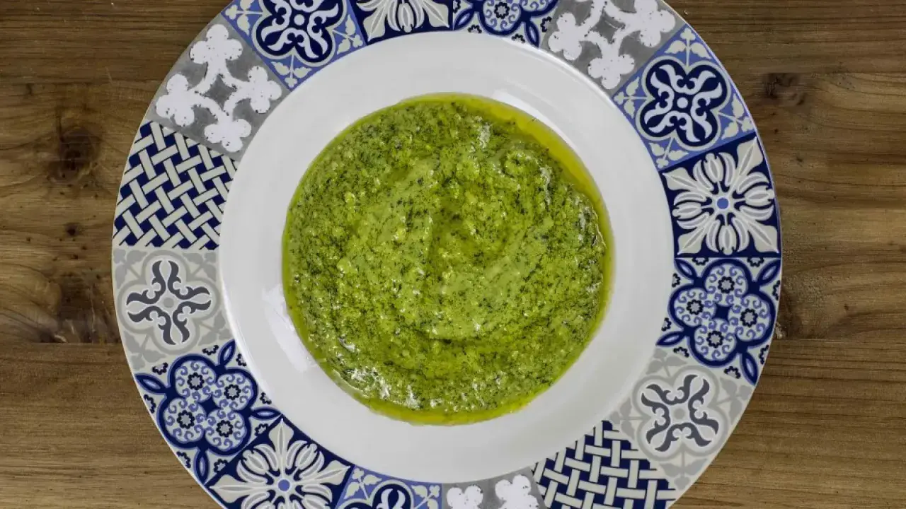 Un plato blanco con un borde decorado con azulejos presenta una generosa porción de vibrante salsa pesto, lista para realzar cualquier plato.