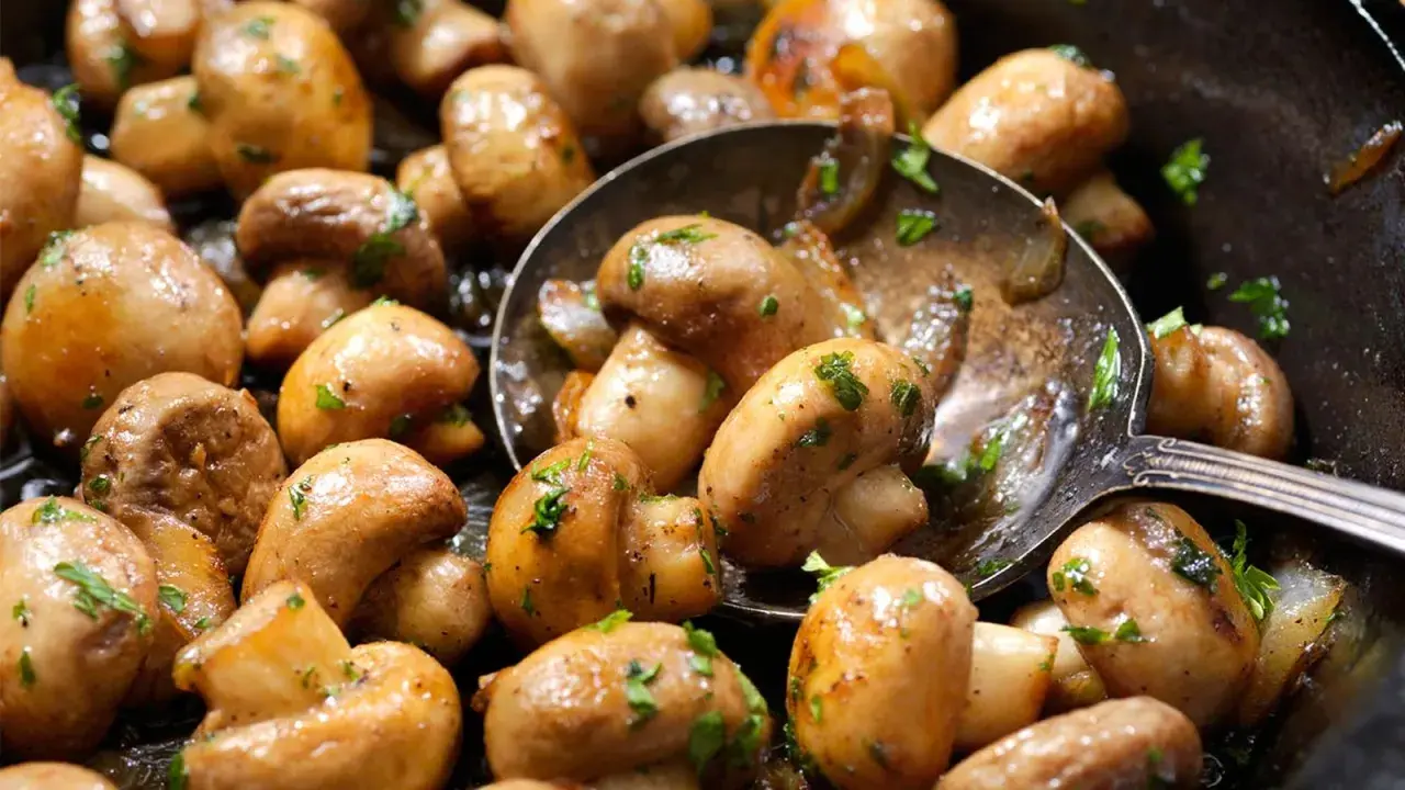 Champiñones salteados con perejil, perfectos para tus recetas con champiñones. Una cuchara sirve para cogerlos.