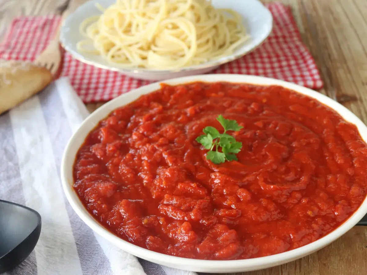 Un tazón de vibrante salsa arrabiata, decorado con perejil, junto a espaguetis y pan.