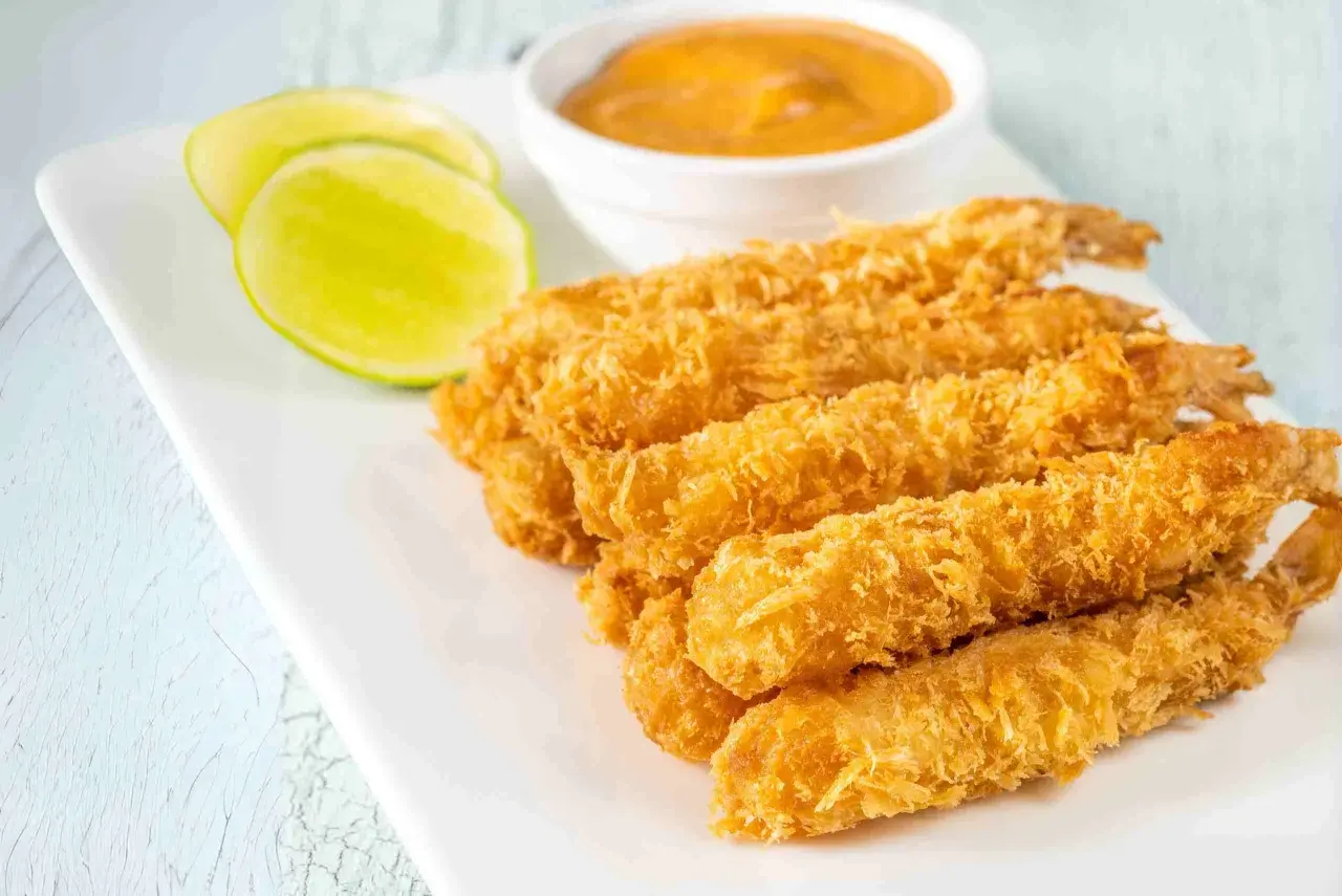 Crujientes gambas a la gabardina doradas, servidas con rodajas de lima y una salsa cremosa.