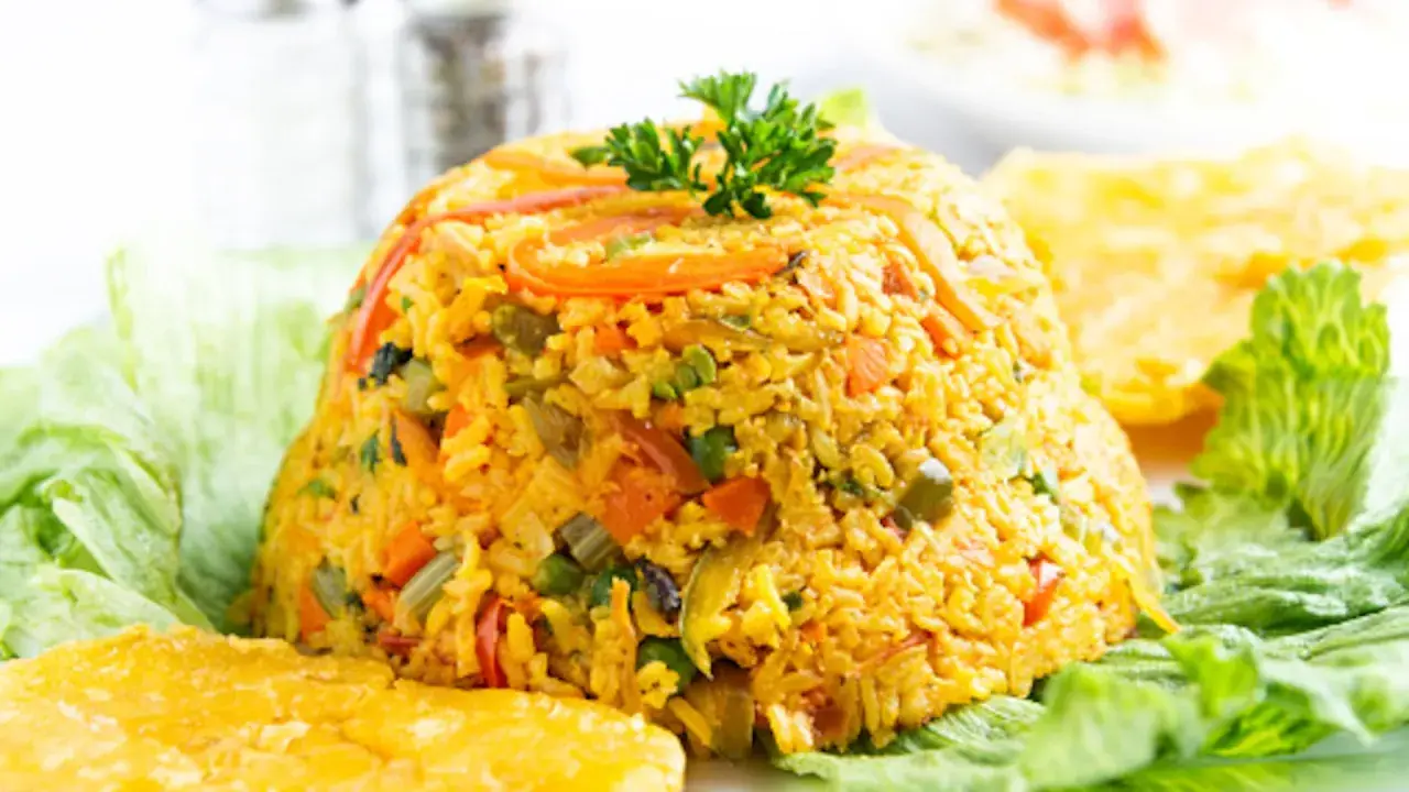 Un montículo de arroz con pollo, adornado con perejil, servido sobre hojas de lechuga y acompañado de plátanos fritos.