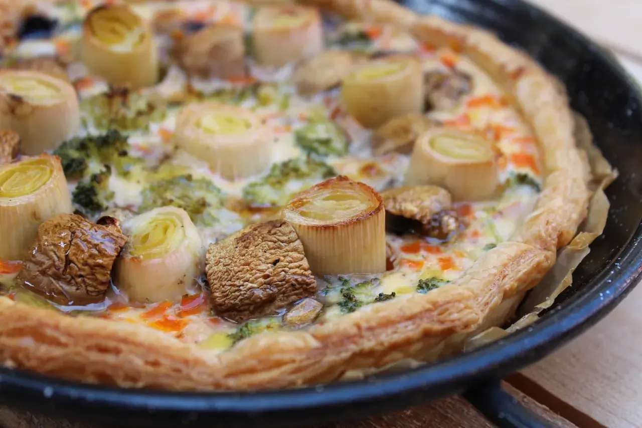 Quiche de verduras recién horneada, con puerros, brócoli y champiñones, lista para disfrutar.