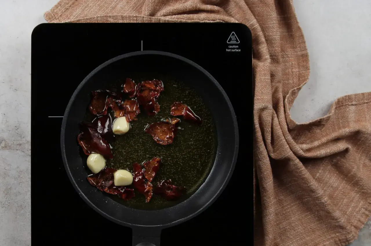 Sartén con aceite, ajos y trozos de pimiento rojo, preparando la base para una salmorreta receta.