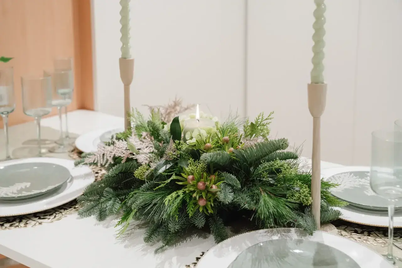Centros de mesa de navidad sencillas con velas y follaje verde. Copas y platos listos para una cena festiva.
