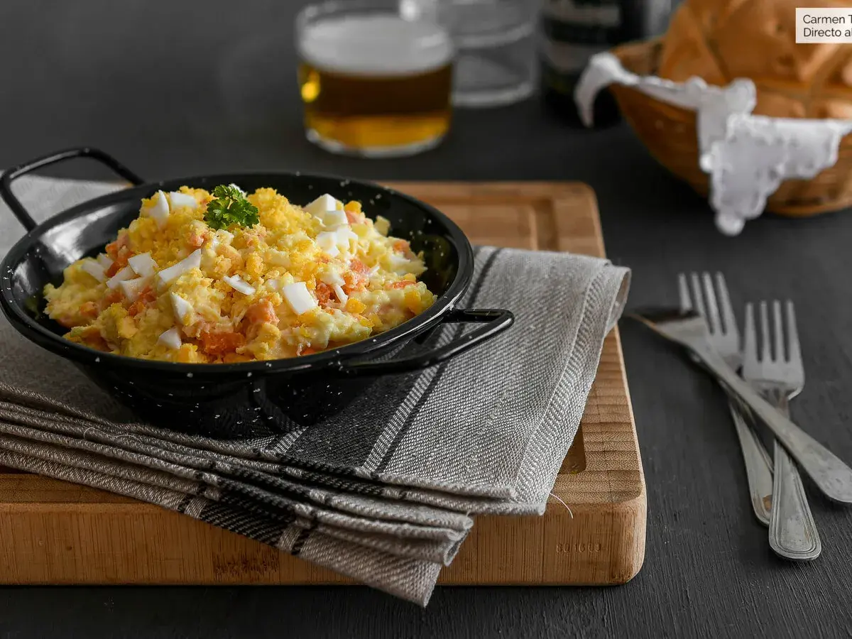 Deliciosa ensaladilla rusa en un cuenco negro, con huevo duro picado y perejil. Acompañada de pan y cerveza.