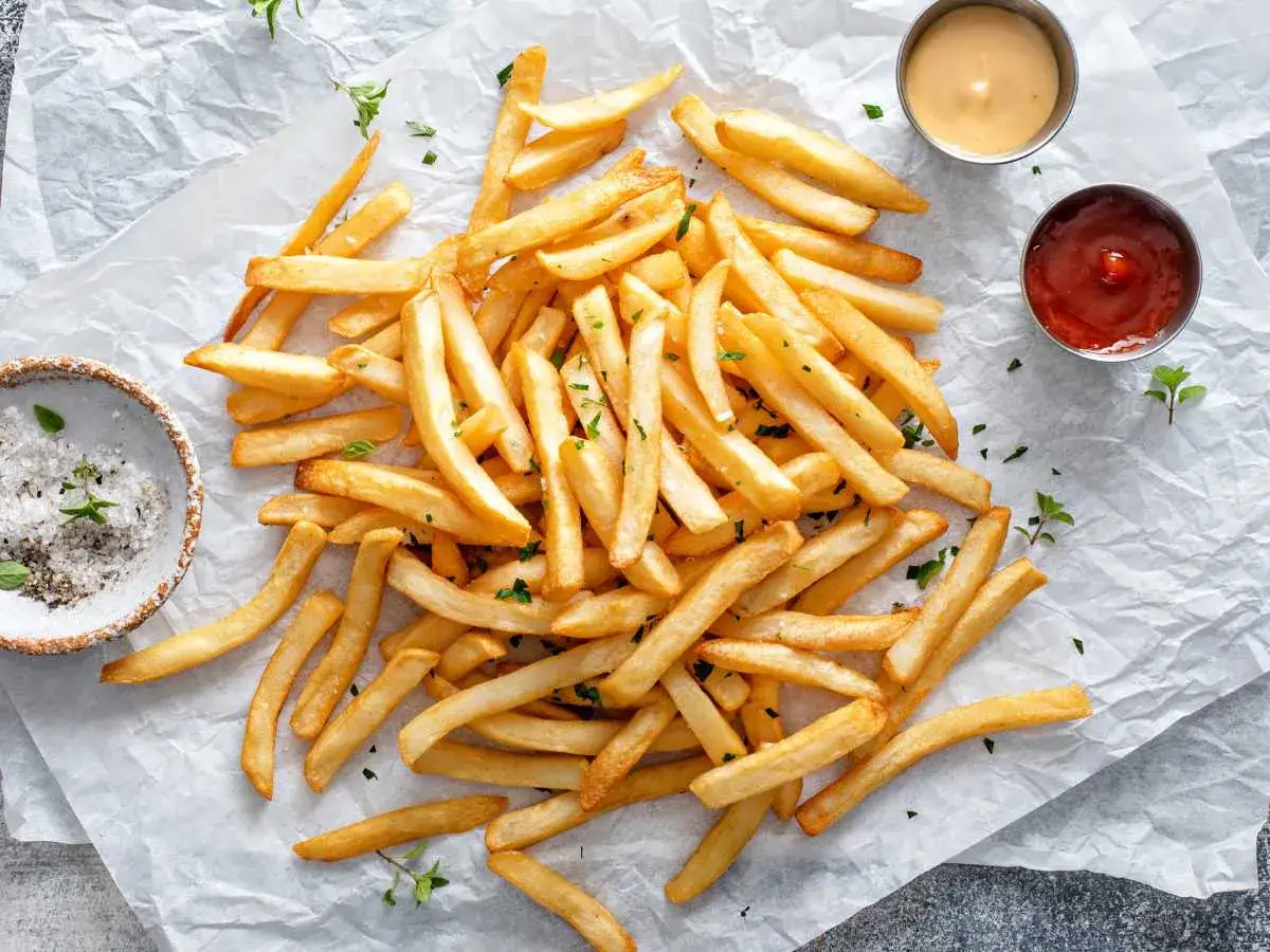 Mont&oacute;n de patatas fritas airfryer doradas y crujientes, espolvoreadas con perejil picado, junto a un cuenco de sal y dos salsas.