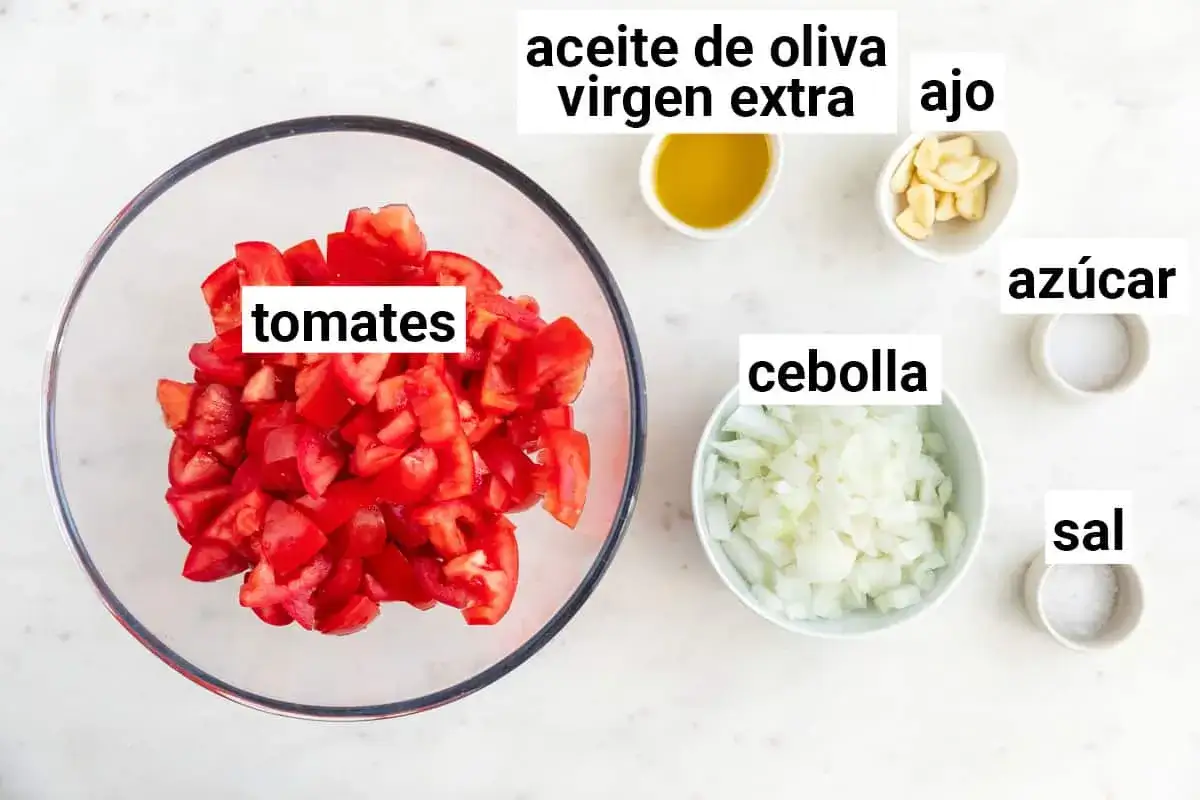 Ingredientes para una deliciosa salsa de tomate casera: tomates picados, cebolla, ajo, aceite de oliva virgen extra, azúcar y sal.